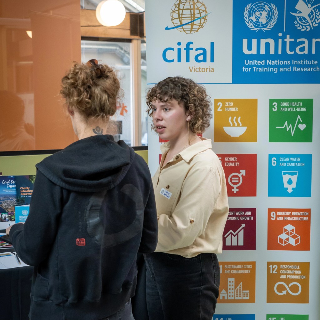 CIFAL Victoria Program Officer Bethany Woodbridge speaking to a guest at the CIFAL Victoria table at the Salish Sea Hub Launch Event in May 2025.
