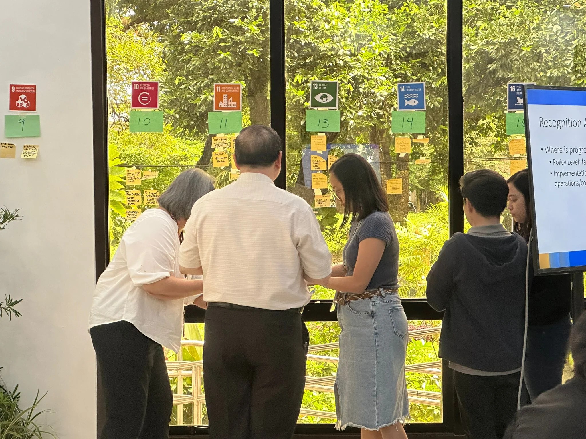 Four executives from Mahidol University in Bangkok, Thailand place sticky notes on a window while participating in in the "Developing a Sustainability Mindset" course. 