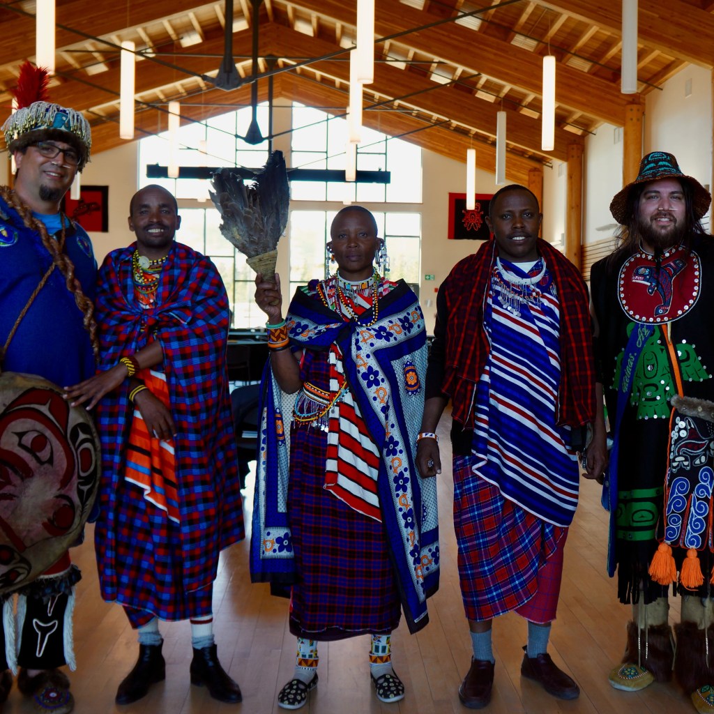 Representatives of the Maasai from Tanzania and First Nations from British Columbia and the Yukon pose together in a large room in the Yukon, Canada.
